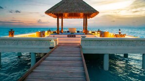 A wooden pier leading to a thatched-roof structure with seating and a sign reading 'Sol of Sea.'