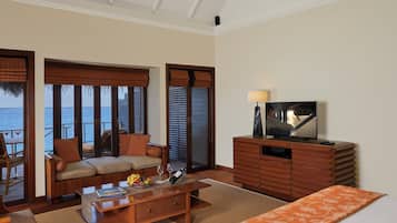 Una stanza con un divano, un tavolino da caffè con libri e una bottiglia, una televisione su un mobile in legno e vista mare attraverso ampie finestre.