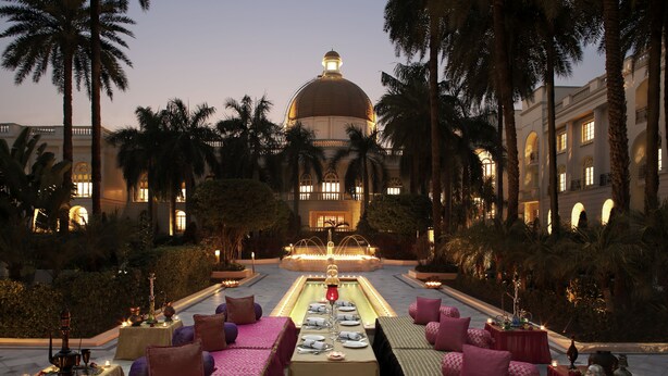 A luxurious outdoor dining area with tables set for a meal, surrounded by palm trees and a grand building in the background. - Taj Mahal Lucknow (Lucknow)