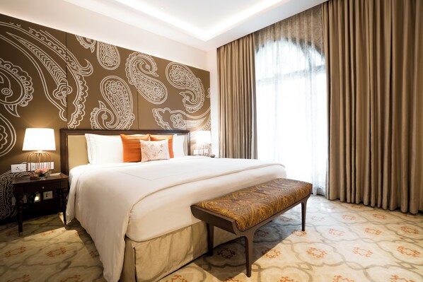 A hotel room with a large bed, a bench, a nightstand, and a wall with paisley patterns.