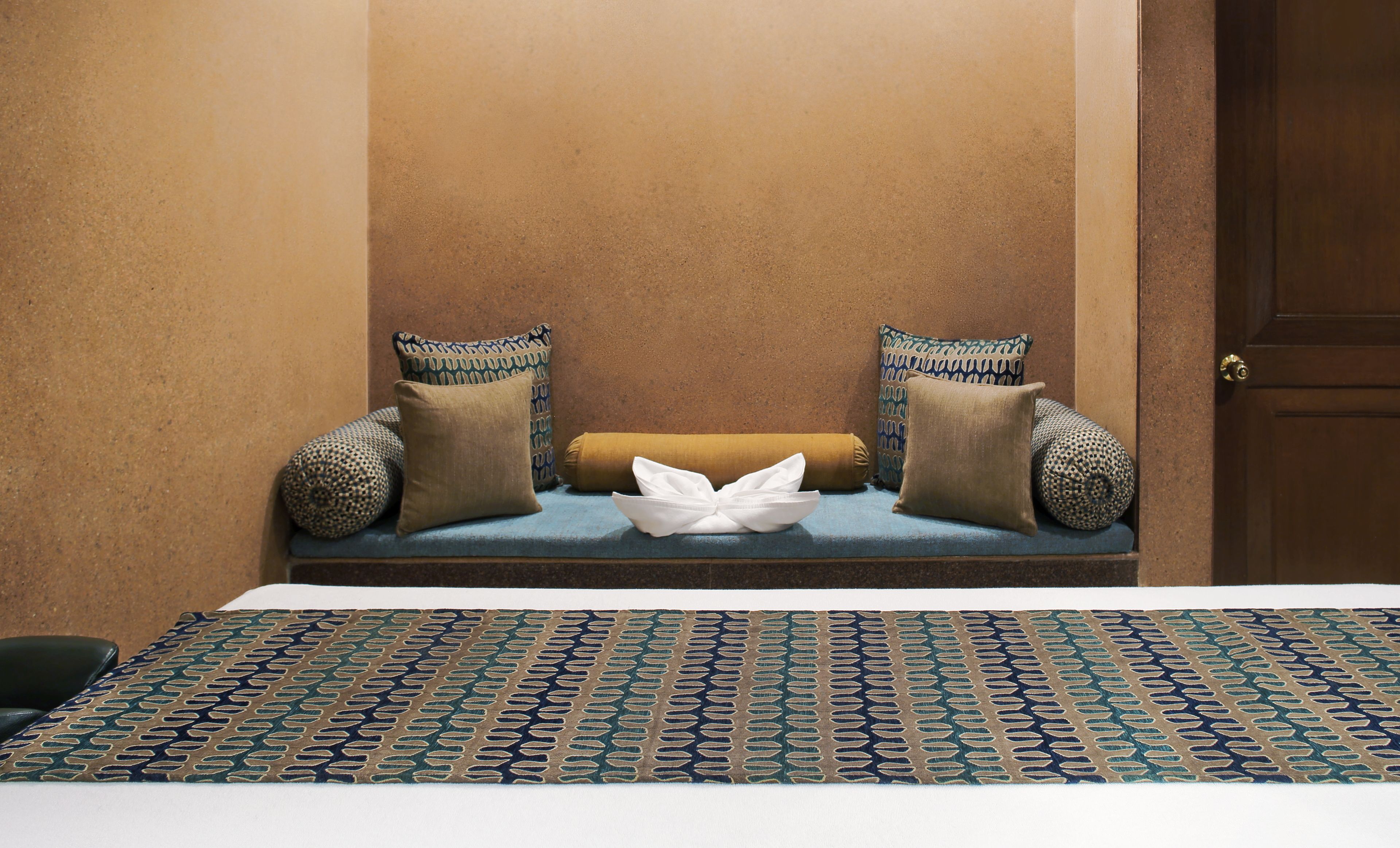 A room with a bench against a textured wall, two patterned pillows, and a patterned rug.