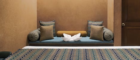 A room with a bench against a textured wall, two patterned pillows, and a patterned rug.