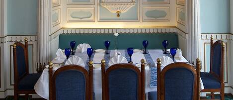 Comedor con candelabro, paneles de pared ornamentados y una mesa puesta para seis personas con sillas azules.
