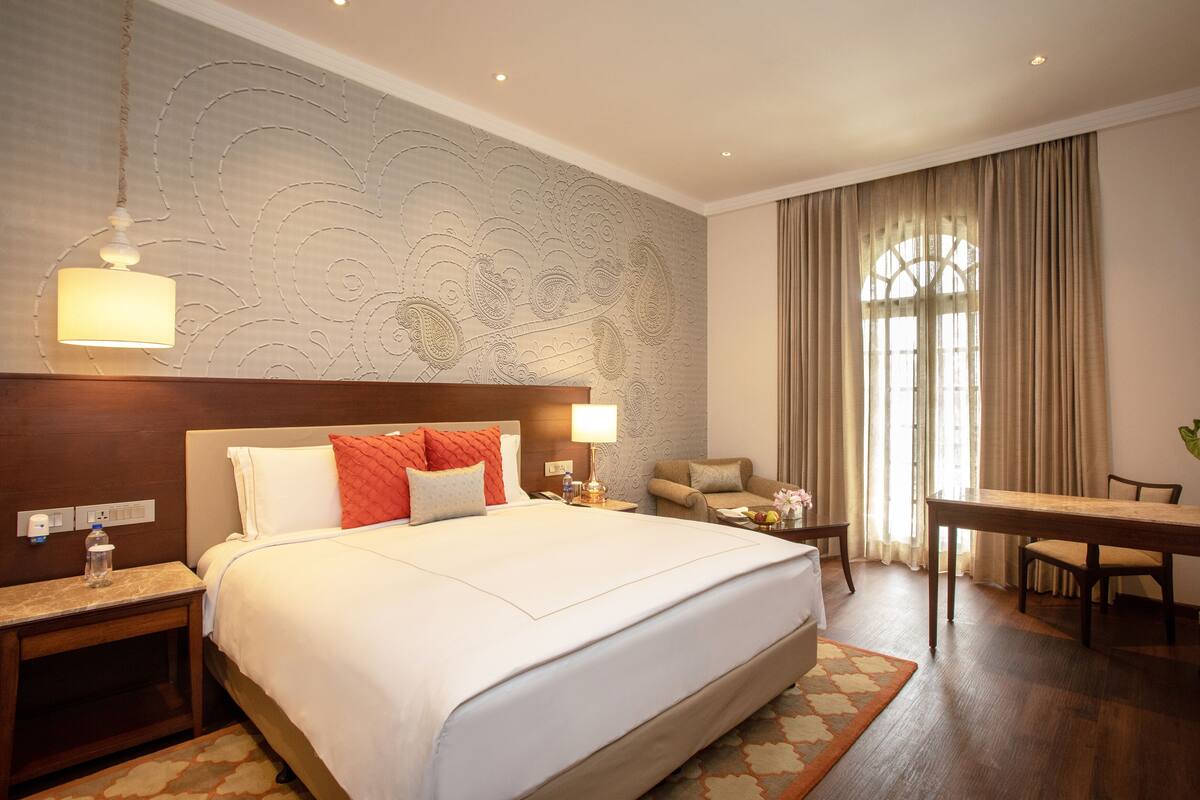 A hotel room with a large bed, a desk, a chair, and a dining table.