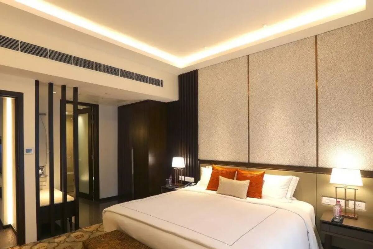 A hotel room with a large bed, a bench, a nightstand with a lamp, and a wall with a textured pattern.