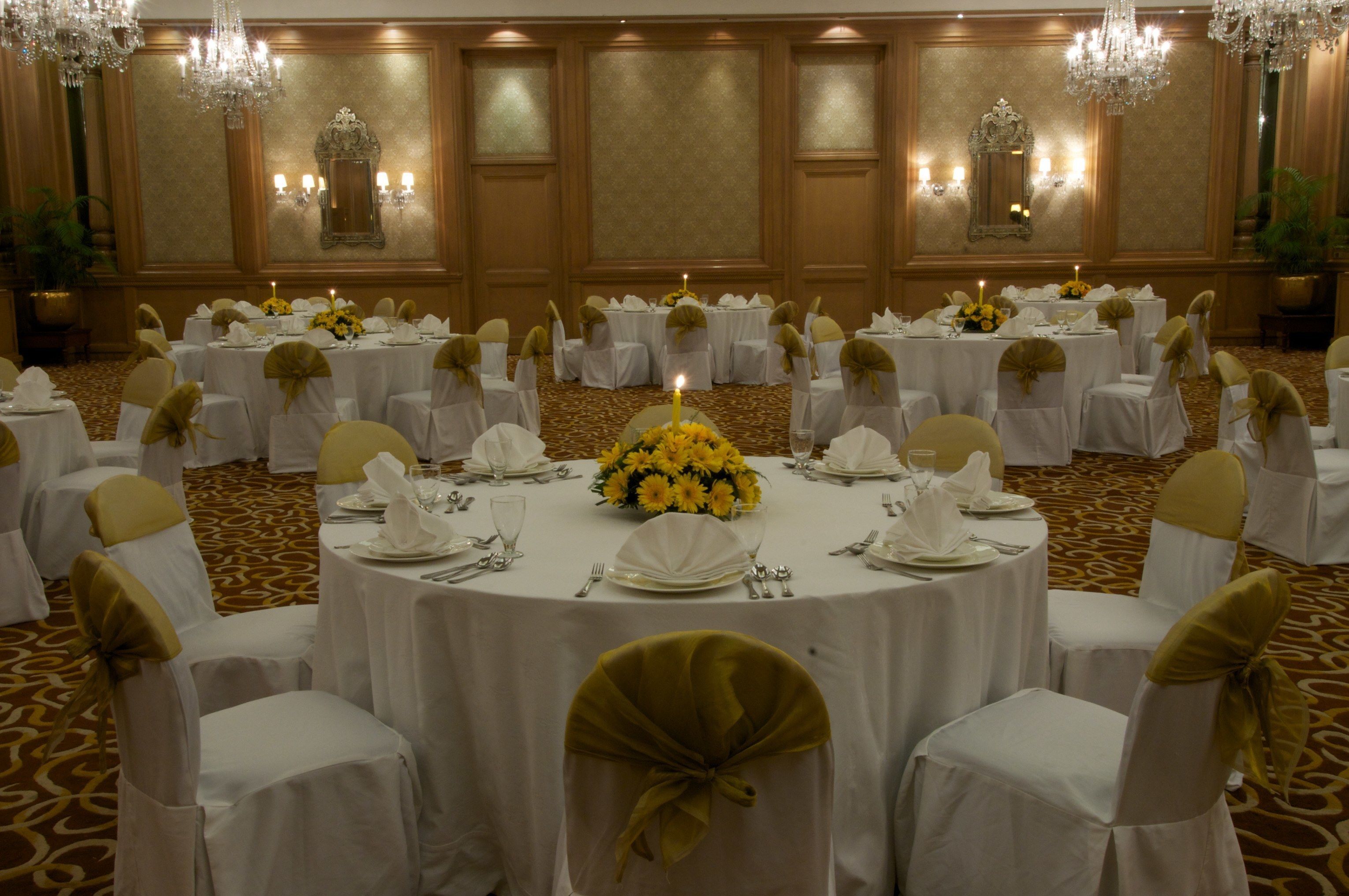 A banquet hall with round tables set for a formal event, featuring chandeliers and floral centerpieces.