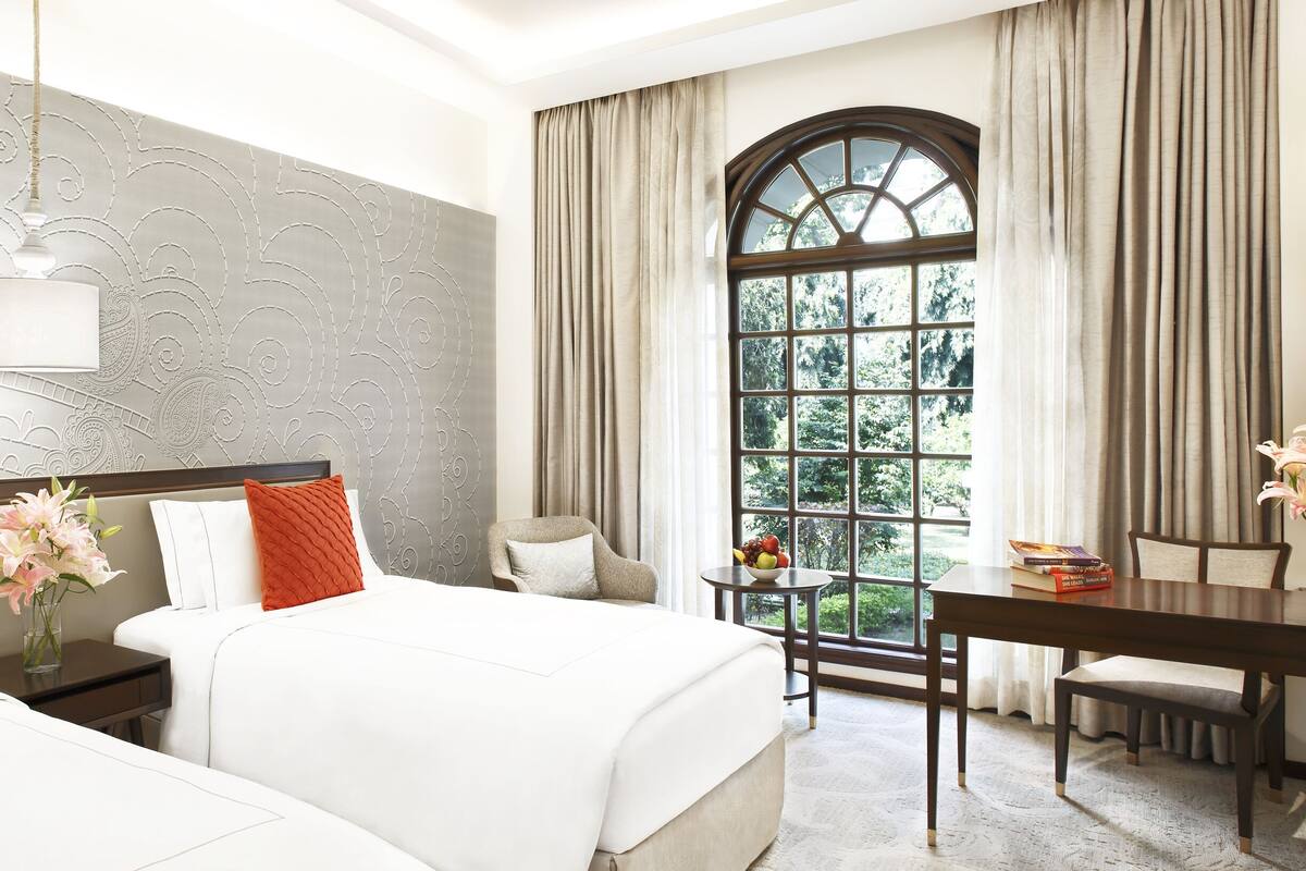 A hotel room with two beds, a desk, a chair, a window with curtains, and a decorative wall.
