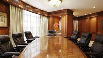 A conference room with a large oval table, leather chairs, wooden paneling, and a chandelier.