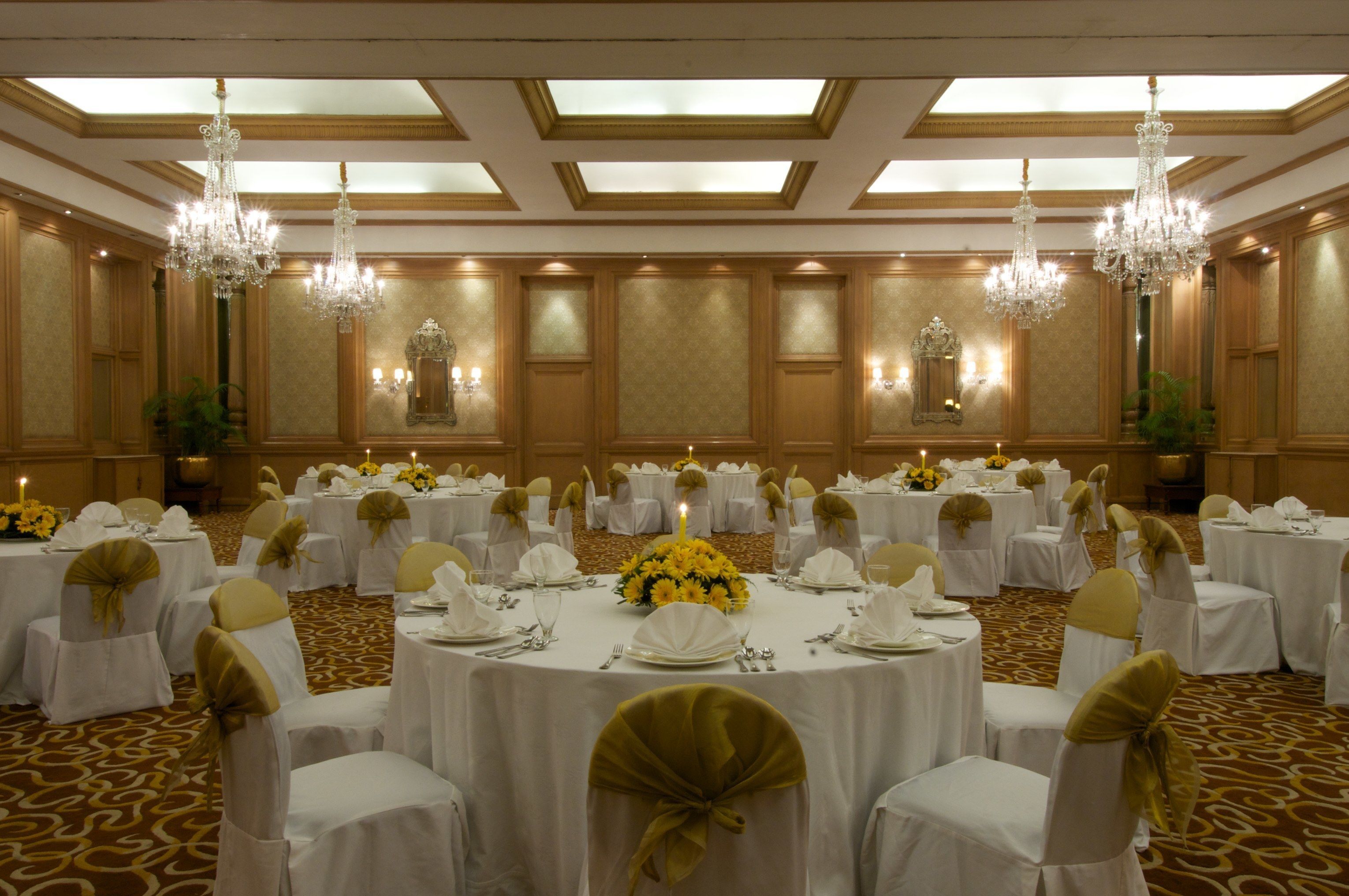 A banquet hall with round tables, chairs, chandeliers, and floral centerpieces.