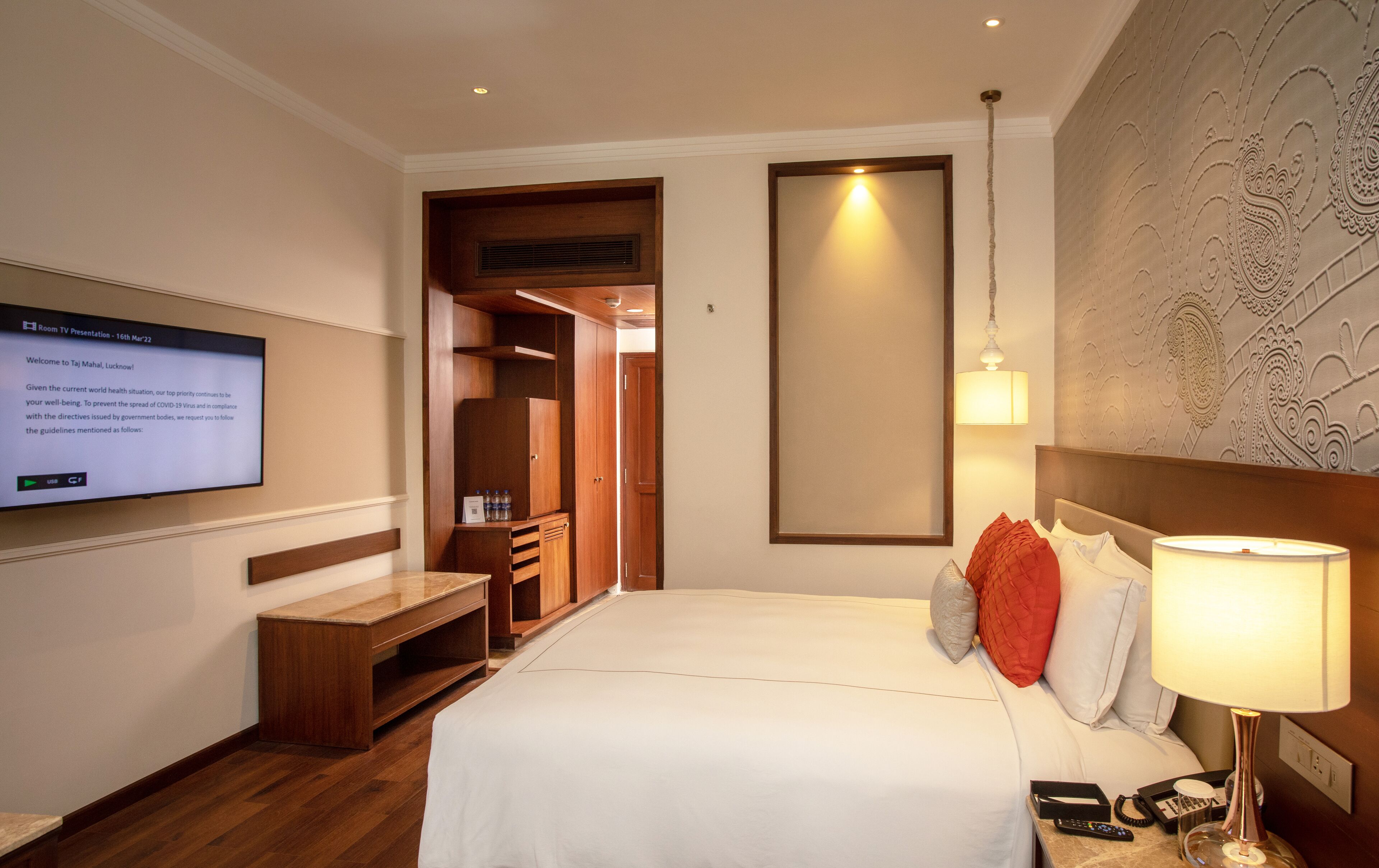 Una habitación de hotel con cama, mesita de noche, lámpara, televisor y armario.