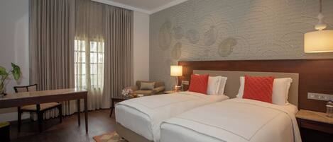 A hotel room with two beds, a dining table, a sofa, and a large window with curtains.