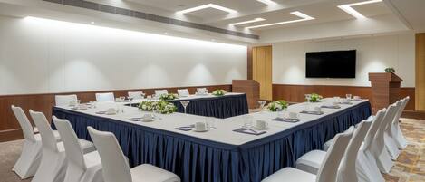 A conference room with a long table, white chairs, and a flat-screen TV on the wall.