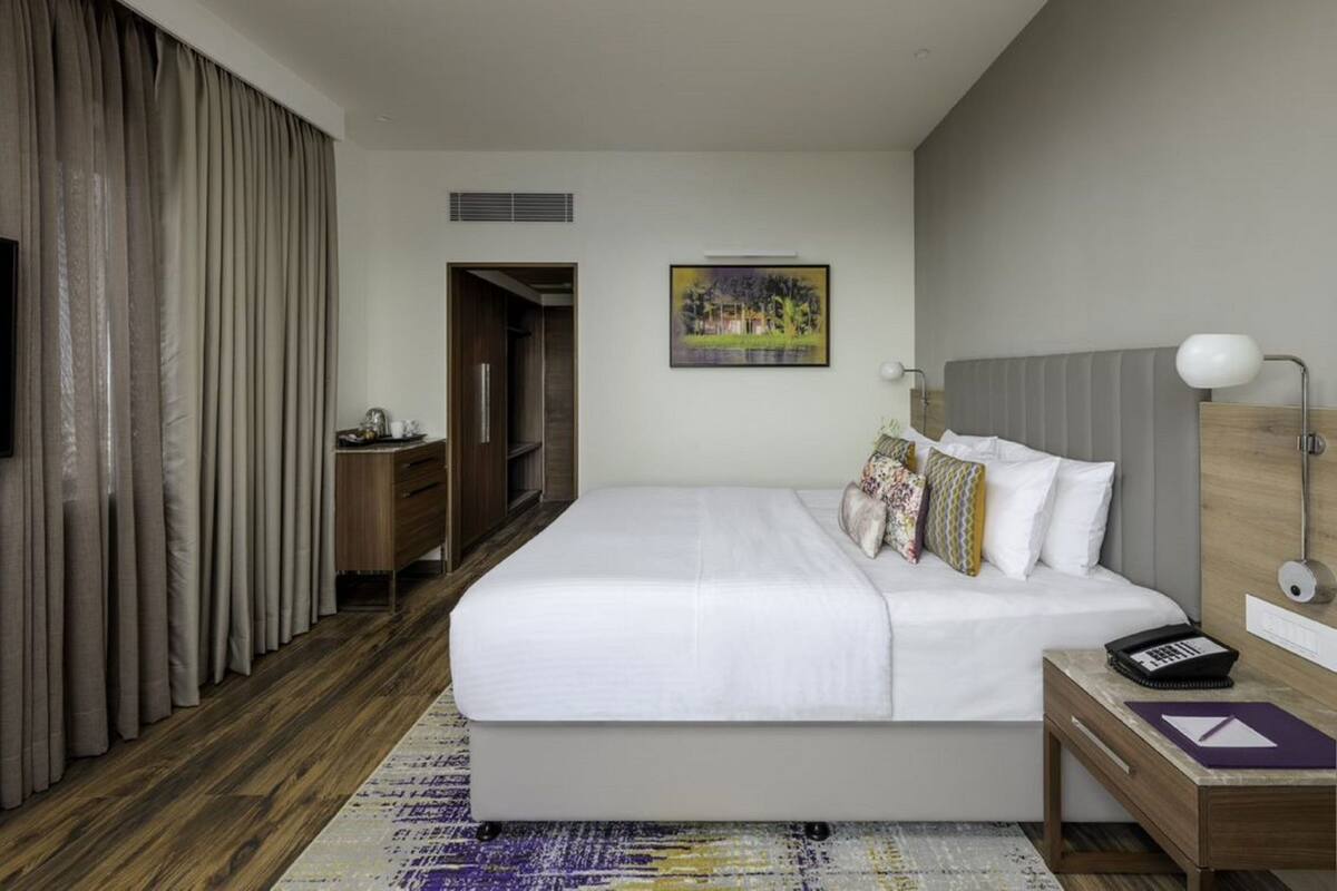 A hotel room with a large bed, bedside table, lamp, and a painting on the wall.