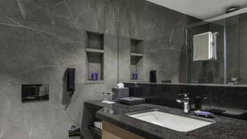 Un baño moderno con pared de mármol, inodoro blanco, lavabo negro y un espejo grande.