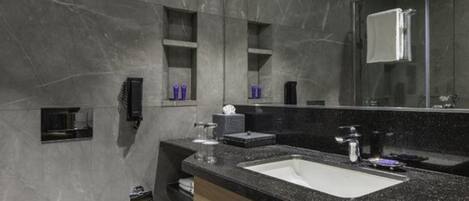 Un baño moderno con pared de mármol, inodoro blanco, lavabo negro y un espejo grande.