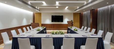 Un salón de conferencias con una larga mesa, sillas blancas y una televisión de pantalla plana en la pared.