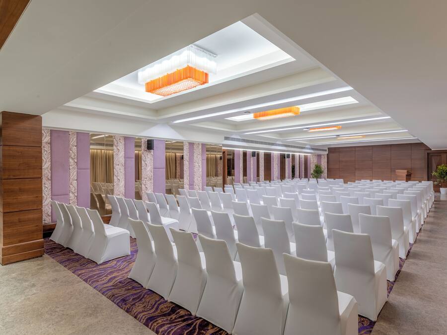 Un salón de conferencias con hileras de sillas blancas, una alfombra estampada e iluminación empotrada en un techo con tragaluces.