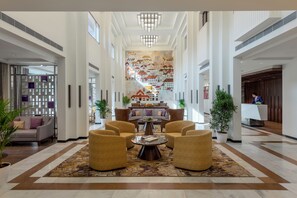 A spacious lobby with a central seating area, a reception desk, and a mural of houses on the wall.