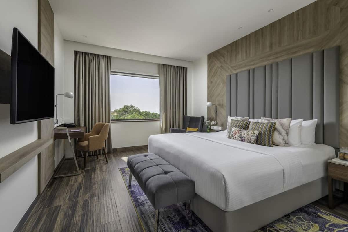 A hotel room with a large bed, a desk with a chair, a television, and a window with curtains.