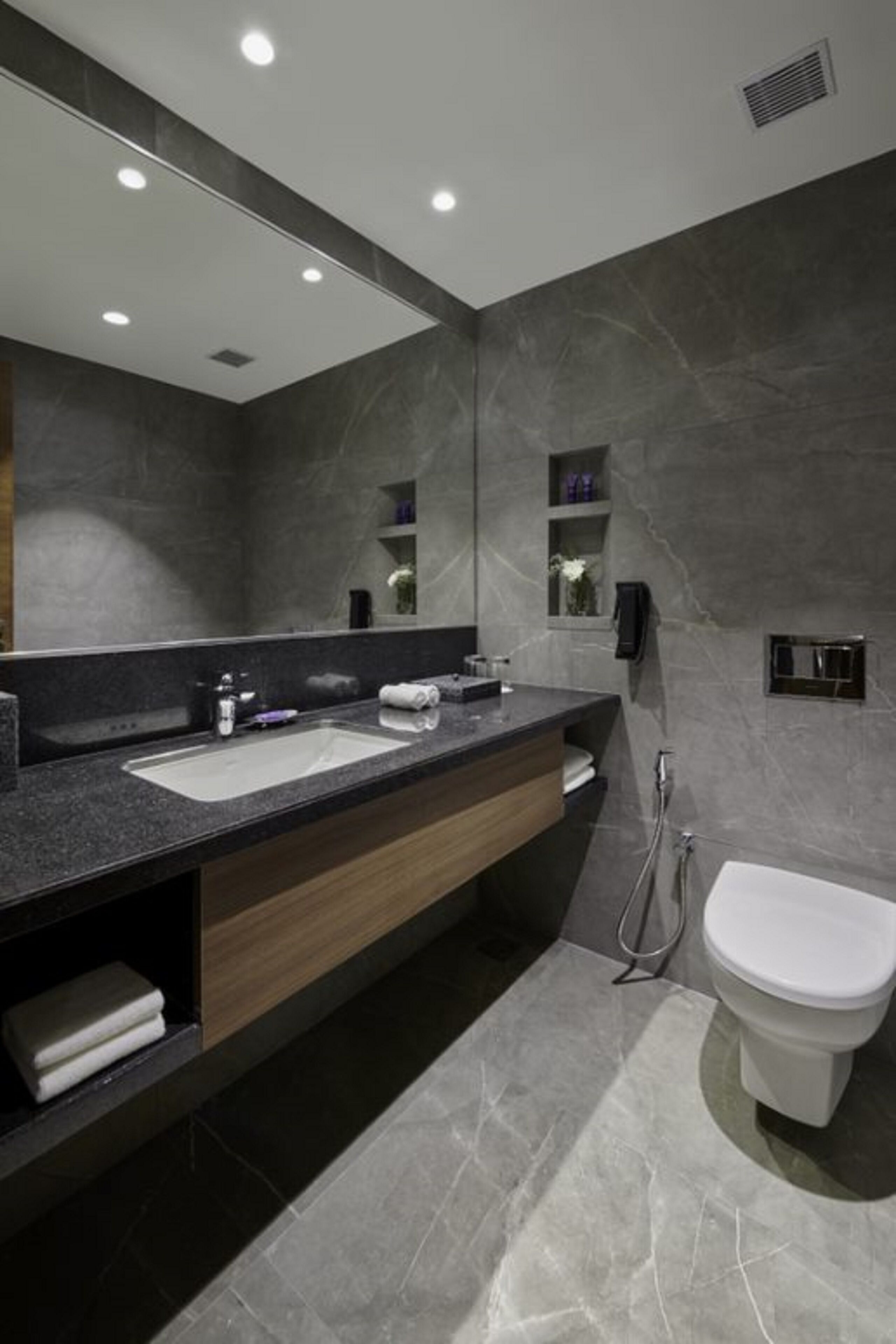 A modern bathroom with a large mirror, dual sinks, a toilet, and a shower.