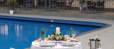 An outdoor dining area with a pool, white tablecloth, and red chair sashes.