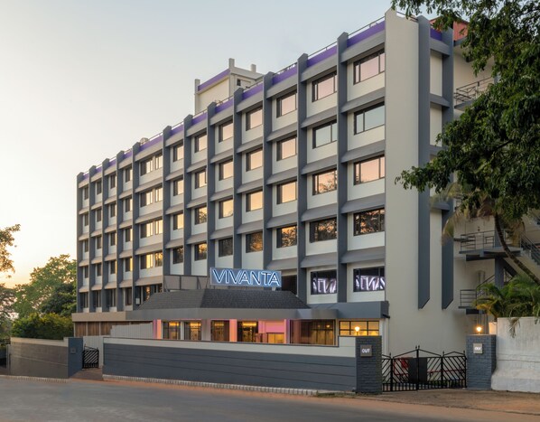 A multi-story hotel with a modern design, featuring a prominent entrance with a neon sign, multiple balconies, and a gated driveway.
