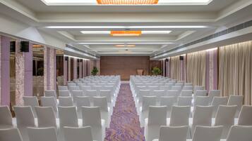 A conference room with rows of white chairs, a patterned carpet, and a ceiling with recessed lighting and a chandelier.