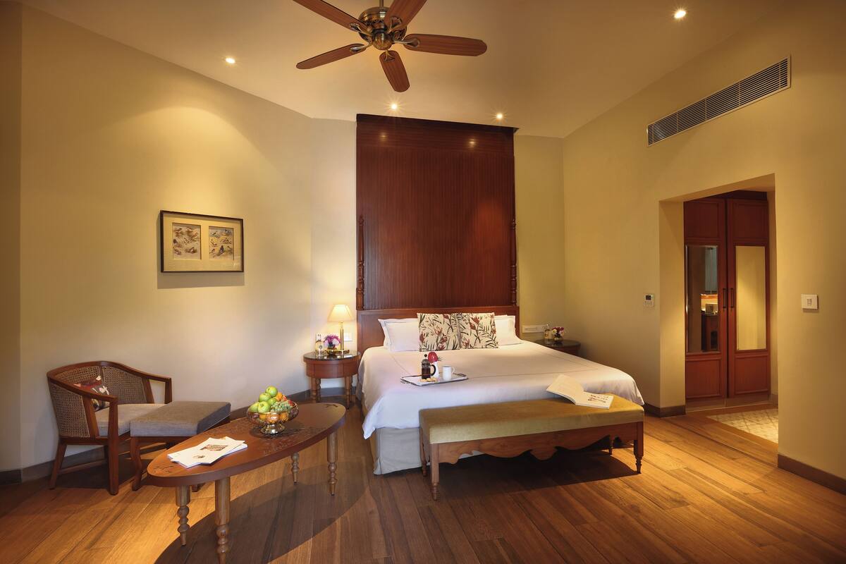 A hotel room with a bed, a desk, a chair, a ceiling fan, and a picture on the wall.