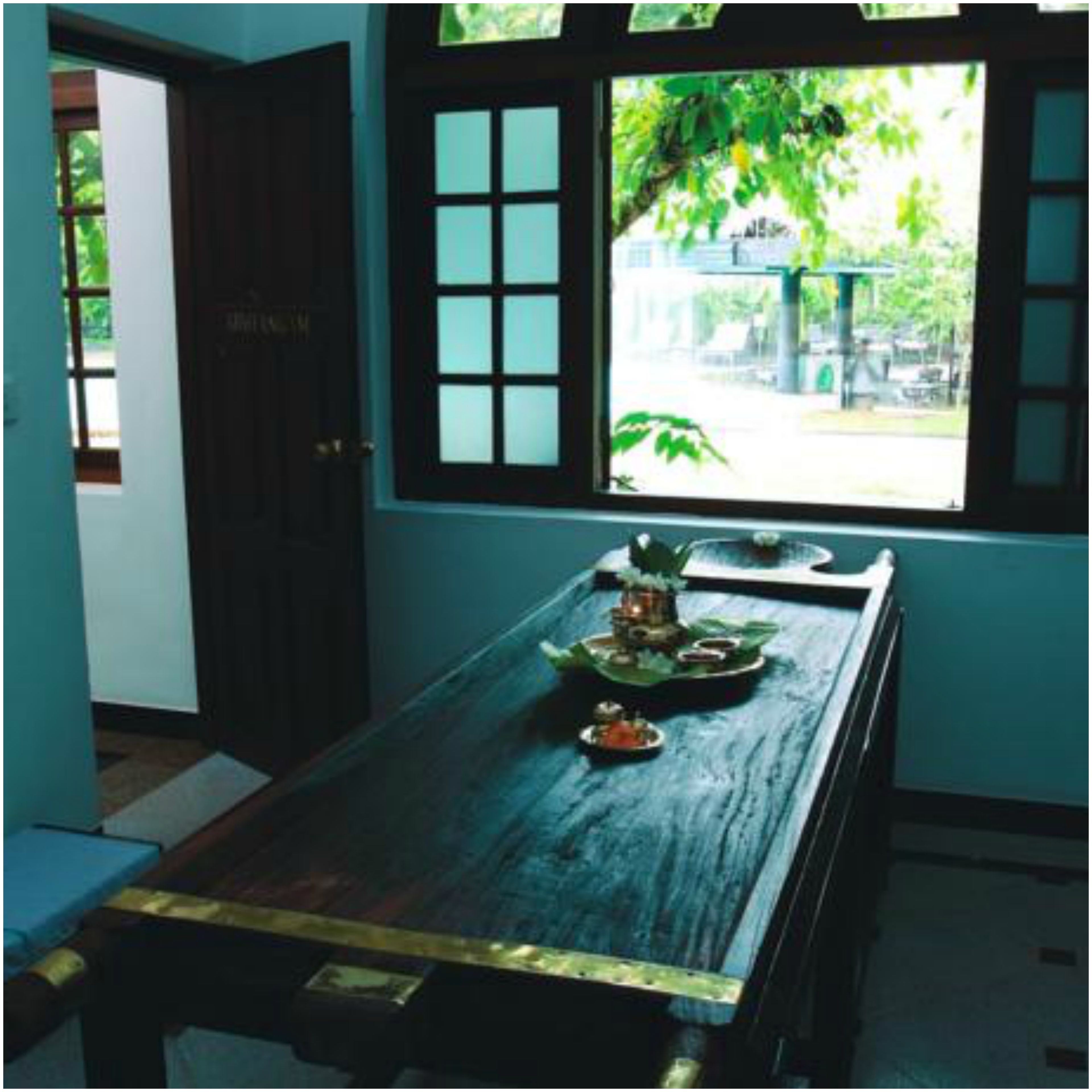 A room with a wooden table, a window with a view of greenery, and a door.