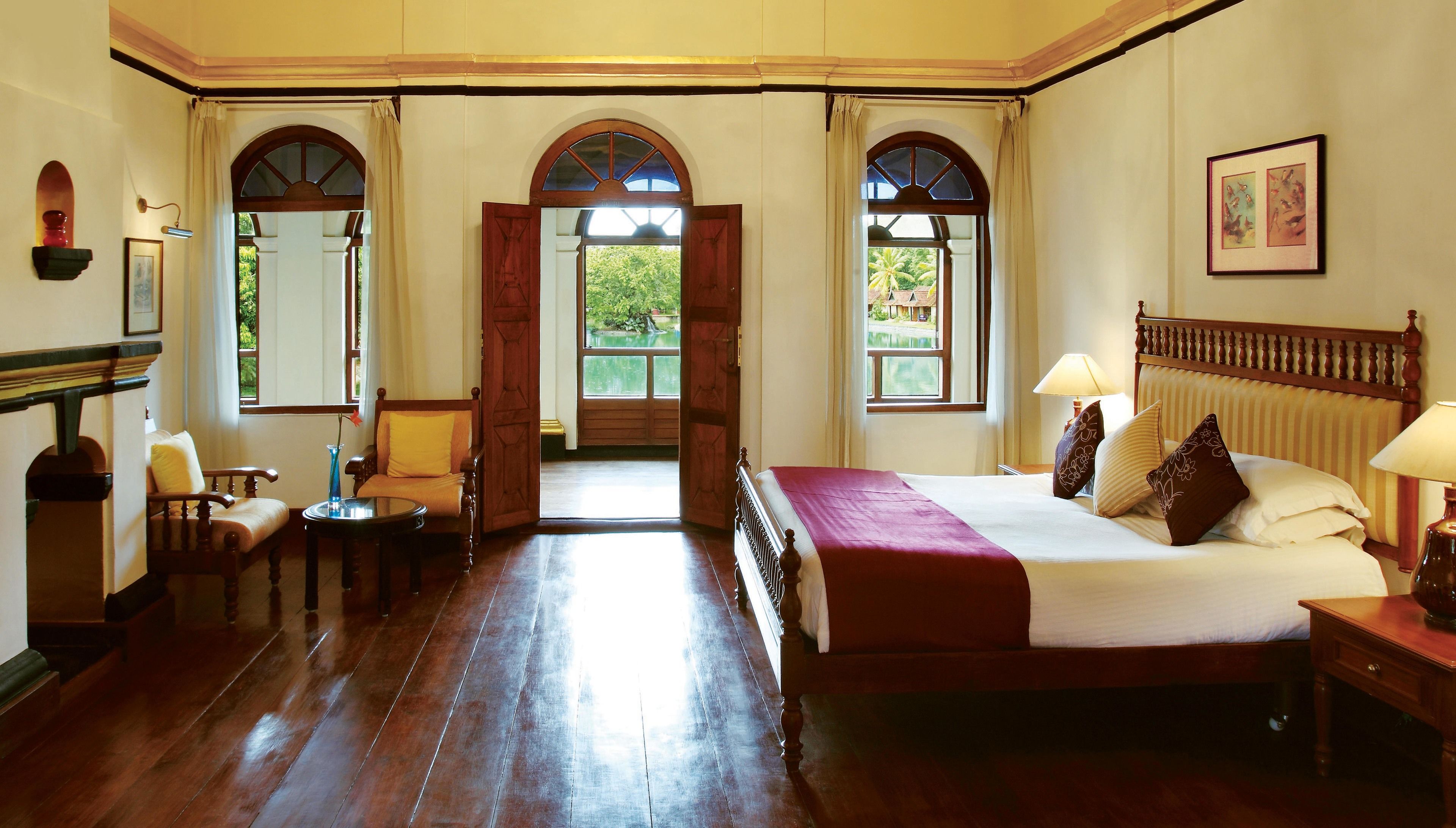 A room with a large bed, a wooden chair, a small table, and a view through an open door to a balcony.