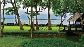 A lakeside park with a wooden bridge, benches, and a bicycle. - Taj Kumarakom Resort & Spa, Kerala (Kottayam)