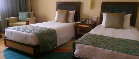 A hotel room with two single beds, a chair, a nightstand, and a lamp.
