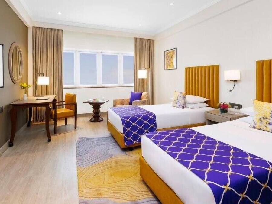 A hotel room with two beds, a desk, a chair, a small table, and a window with curtains.
