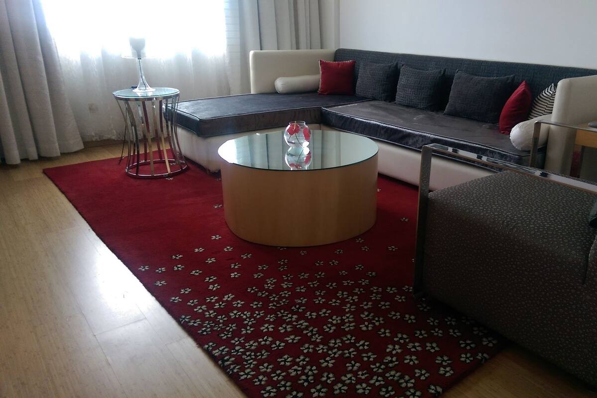 Una sala de estar moderna con un sofá modular, una mesa de centro de vidrio y una alfombra floral roja.