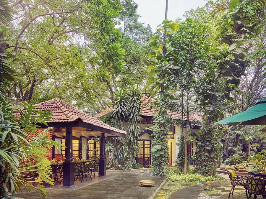 Un patio con zona de estar techada, un sendero y abundante vegetación.