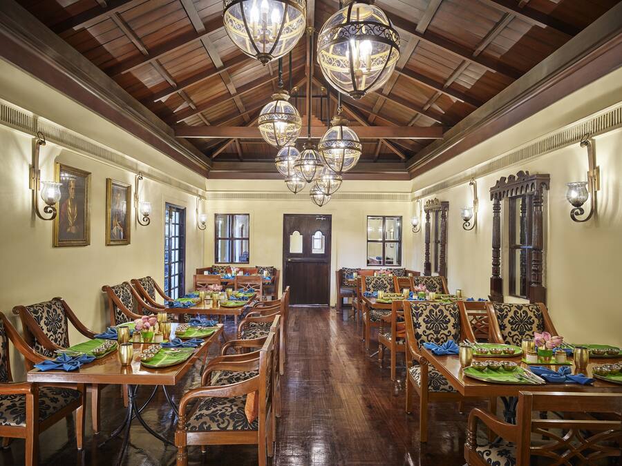 Un comedor espacioso con mesas y sillas de madera, candelabros ornamentados y cuadros en las paredes.