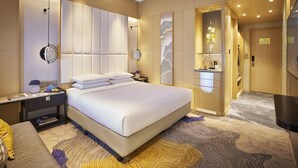 Una habitación de hotel moderna con una cama grande, mesitas de noche, un tocador con espejo y una pequeña zona de estar.