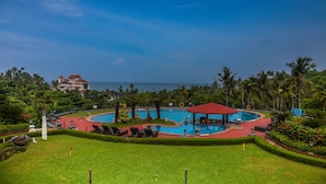 Un resort con una amplia piscina circular, palmeras y vista al océano.