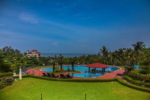 Un resort con una amplia piscina circular, palmeras y vista al océano.