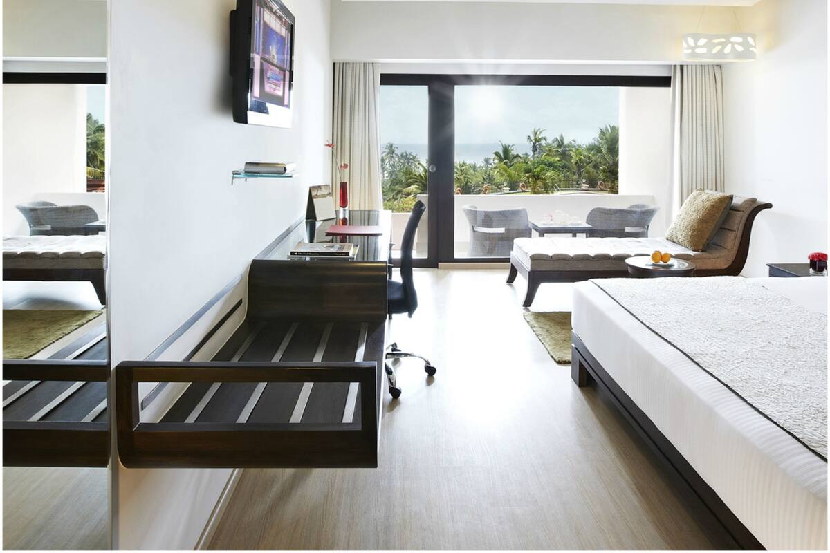 A modern hotel room with a bed, a desk, a chair, and a view of the outdoors.