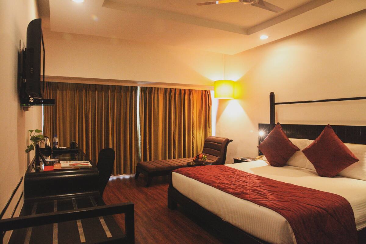A hotel room with a bed, a desk, a chair, a TV, and a lamp.