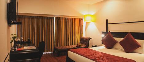 A hotel room with a bed, a desk, a chair, a TV, and a lamp.