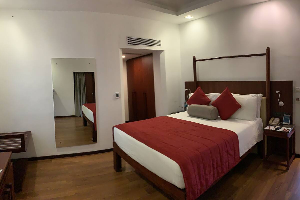 A four-poster bed with a red bedspread, a bedside table with a phone, and a mirror on the wall.
