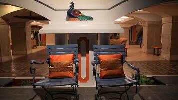 A lobby with two blue chairs with orange cushions, a decorative peacock sculpture, and a central pillar with a geometric design.