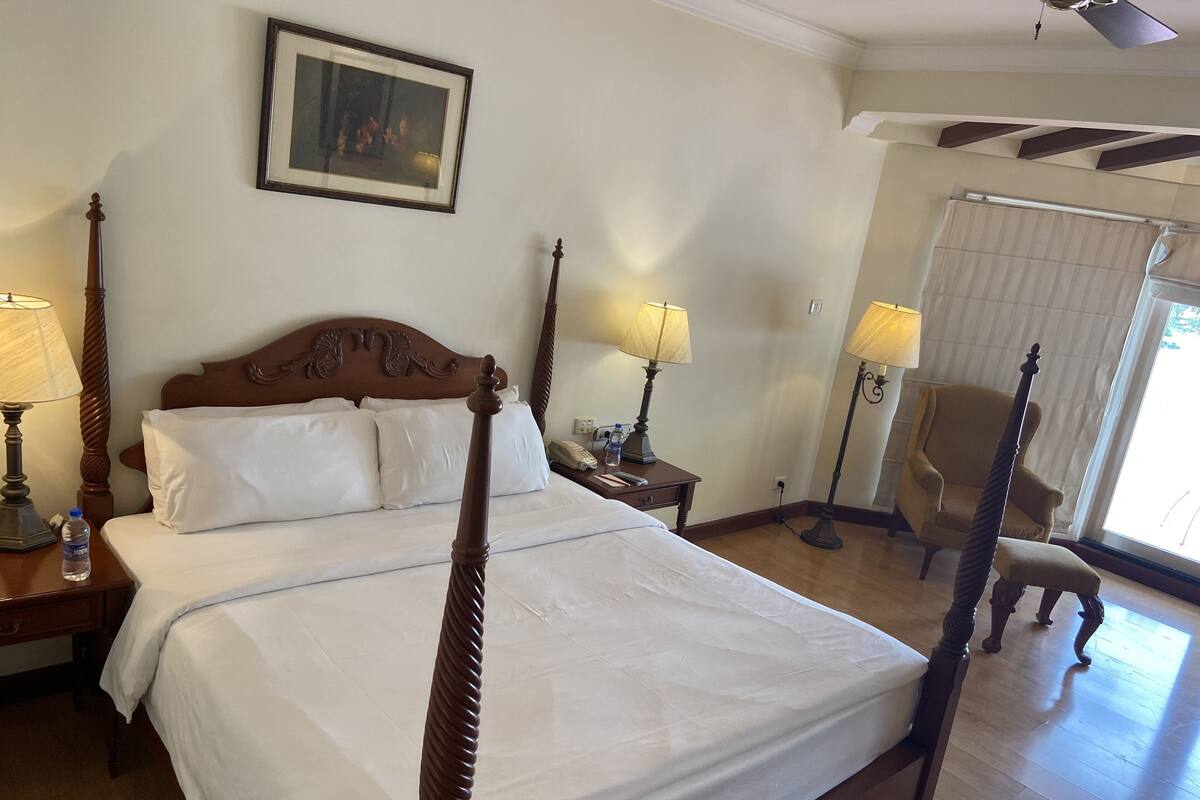 Une chambre d’hôtel avec un lit à baldaquin, deux tables de chevet avec des lampes, une chaise et un tableau au mur.