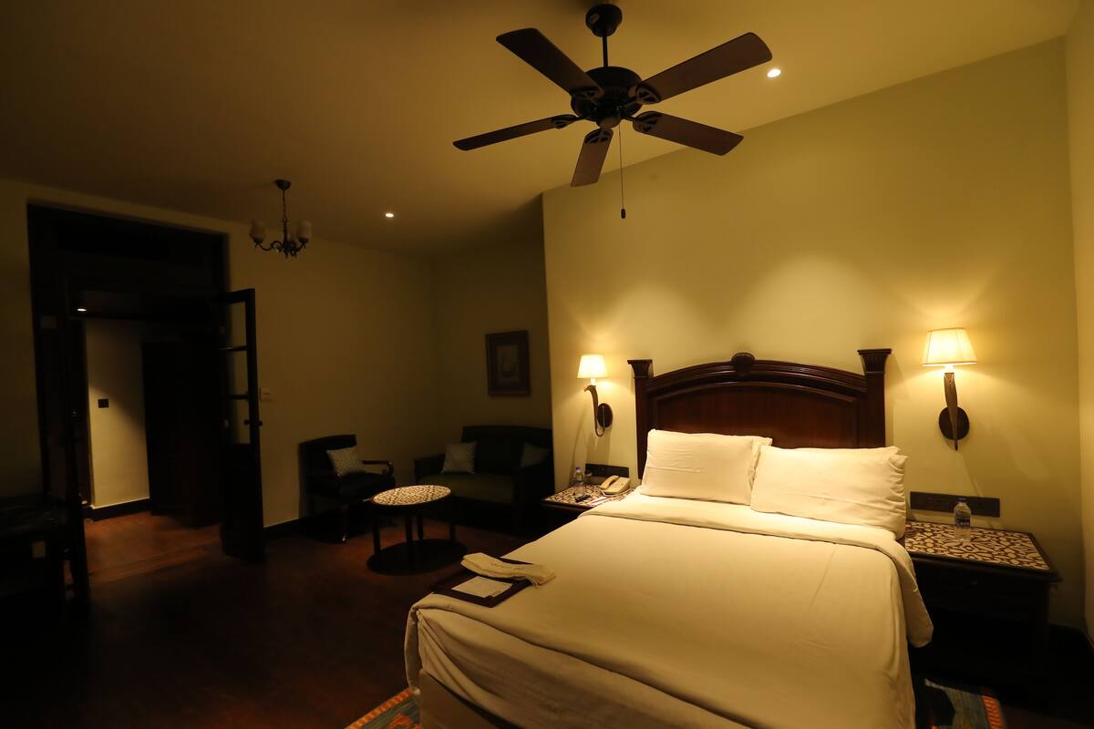 Une chambre d’hôtel comprenant un lit, deux lampes de chevet, un ventilateur de plafond, une table de chevet, une chaise et une petite table.