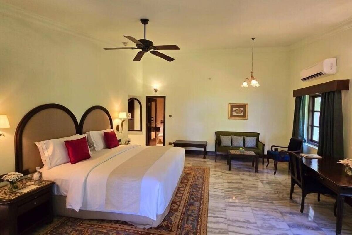 Une chambre d’hôtel avec un grand lit, un bureau, une chaise, un ventilateur de plafond et une fenêtre avec des rideaux.
