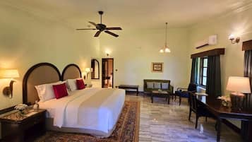 A hotel room with a large bed, a desk, a chair, a ceiling fan, and a window with curtains.