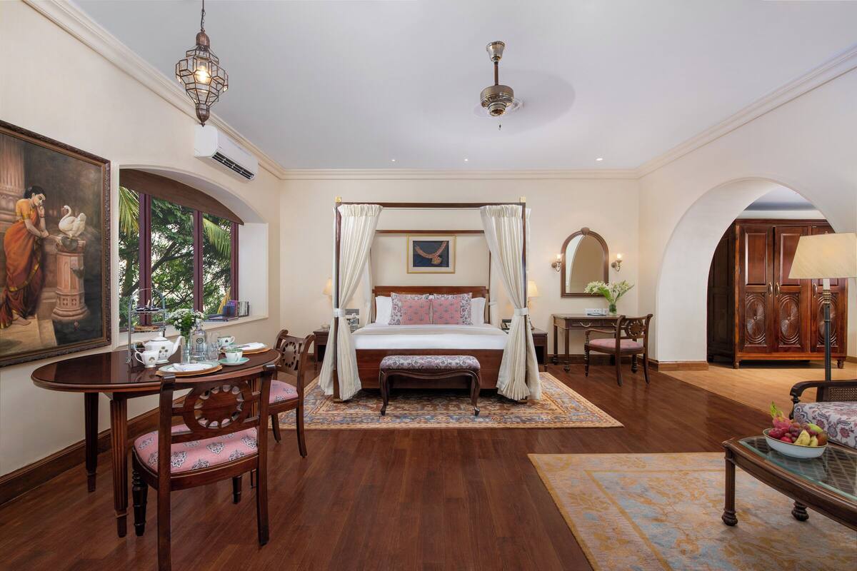 Une chambre spacieuse avec un lit à baldaquin, un coin repas avec une table et des chaises, et un coin salon avec un canapé.