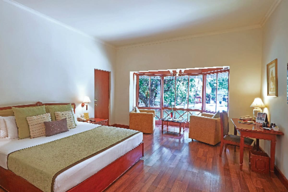 Een hotelkamer met een groot bed, een zithoek met een tafel en stoelen, en een raam met uitzicht op groen.